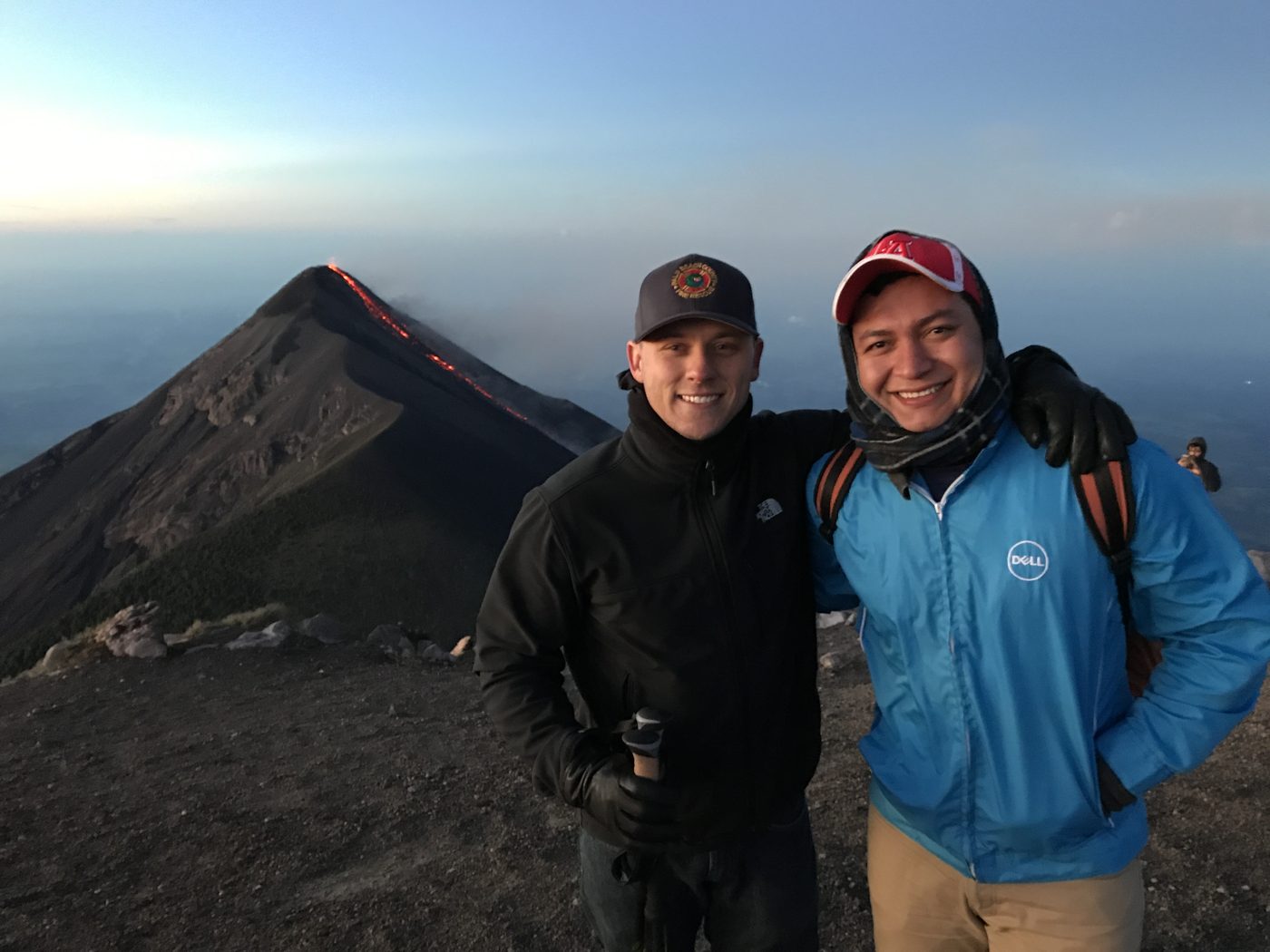 Bidwell Cranage on a volcano summit in Guatemala at sunrise with the Fuego volcano erupting behind him